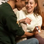 Nuori nainen istuu sohvalla kaukosäädin kädessään ja katsoo televisiota raskausviikot-ohjelmansa aikana.